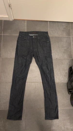 Mörkblå/grå skinny jeans från Nudie Jeans - Snygga mörkblå/grå jeans från Nudie Jeans med klassisk femficksdesign och smal passform. Jeansen har dragkedja och knapp framtill, samt subtila detaljer på bakfickan. Perfekt för dig som gillar stilrena och tajta jeans.