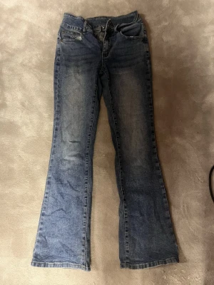 Blå bootcut jeans XS - Säljer ett par klassiska blå bootcut jeans från NF i storlek XS. Jeansen har en snygg tvätt med lätt slitning och femficksmodell. Perfekta för dig som gillar en lite vidare passform nedtill.