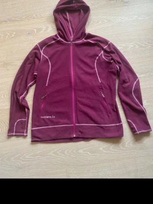 Magenta fleecehoodie från Norrøna XL - Magenta hoodie från Norrøna i fleece med hel dragkedja och huva. Snygga kontrastsömmar i ljusrosa och två fickor med dragkedja framtill. Perfekt för kyliga dagar och outdoor vibes.