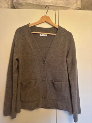 Beige stickad kofta från Wera - Säljer denna mysiga stickade kofta från Wera med v-ringning, koftan har stora ribbade fickor framtill och knappar. Långärmad modell med ribbade muddar vid ärmslut och nederkant. Perfekt för lager på lager under kyliga dagar. Original priset är 900 kronor 
