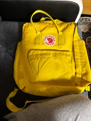 Gul fjällräven väska medium  - Säljer en ikonisk gul Kånken ryggsäck från Fjällräven. Klassisk fyrkantig form med handtag upptill, justerbara axelband och en stor ytterficka med dragkedja. Tillverkad i slitstark syntet och har den välkända runda loggan framtill. 
