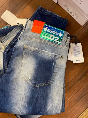  blå jeans med slitningar - Säljer ett par blå jeans ,  coola slitningar och blekta detaljer. Jeansen har en klassisk femficksmodell, synliga stänk och patchar,. Materialet är jeans i bomull och passformen är normal med raka ben.