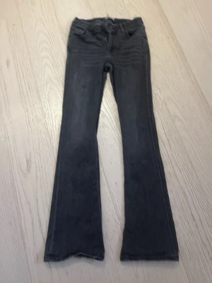 Mörkgrå bootcut jeans - Snygga mörkgrå jeans med bootcut passform och klassisk femficksdesign. Jeansen har dragkedja och knapp framtill samt bälteshällor. Materialet är jeans i bomull och de har en tvättad look som ger en cool vibe.