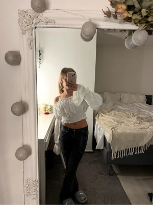 Vit offshoulder croppad blus - Säljer en vit blus med offshoulder och långa puffiga ärmar. Toppen är croppad och har smockad midja som ger en snygg passform. Perfekt för dig som gillar romantisk och trendig stil.