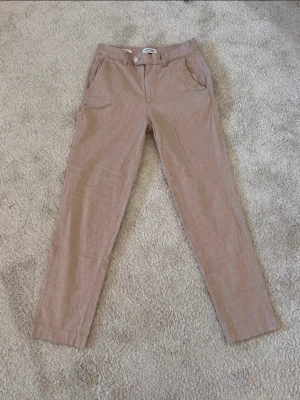Begie linne byxor från Jack and Jones  - Säljer ett par snygga beige linnebyxor med raka ben och klassisk passform. Byxorna har framfickor, bälteshällor och knäppning fram. Baktill finns två fickor med knappdetaljer. Perfekta för en avslappnad men stilren look.
