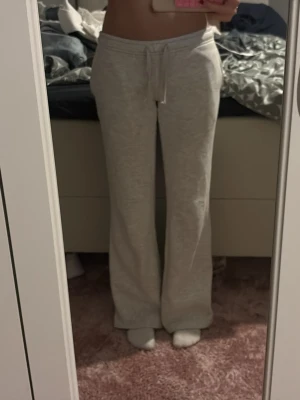 Grå mjukisbyxor med snörning - Säljer ett par ljusgrå mjukisbyxor med snörning i midjan och raka ben. Byxorna har bakfickor och är tillverkade i mjukt bomullsmaterial. Perfekta för chill dagar hemma eller när du vill vara extra bekväm.