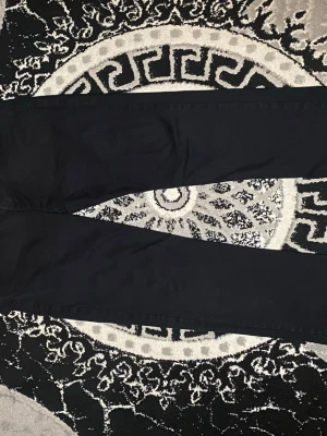 Svarta byxor från Haneton Republic - Säljer ett par svarta byxor från Haneton Republic. De har klassisk femficksdesign, raka ben och knappstängning i midjan. Materialet känns slitstarkt och passar perfekt till en clean och enkel look.