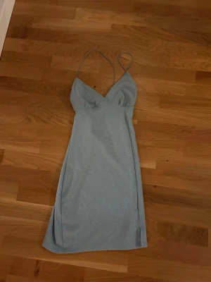 Ljusblå glittrig kort klänning - Supersnygg ljusblå kort klänning från H&M med tunna axelband och glittrigt tyg. Klänningen har en v-ringad urringning och figurnära passform som ger en elegant siluett. Aldrig använd