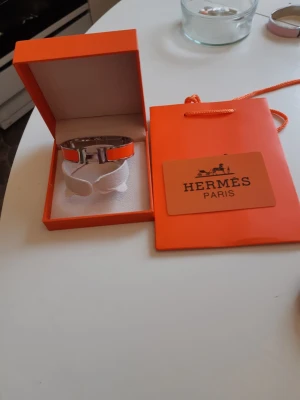 Hermes armband  - Bilderna visar ett Hermès-armband i orange ask och påse, 