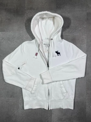 vintage Abercrombie & Fitch zip-up hoodie  - Säljer en vintage Abercrombie & Fitch zip-up hoodie i snygg vit färg. 🧵 Märke: Abercrombie & Fitch 👕 Storlek: Medium 🎨 Färg: Vit 📌 Design: Zip-up hoodie i klassisk Y2K-stil 📍 Skick: Mycket bra, se bilder!  Beskrivning: • Tidlös och eftertraktad vintage-design från Abercrombie & Fitch • Zip-up modell med huva – praktisk och bekväm • Mjuk och skön – perfekt för vardag och layering • Inga fläckar, noppor eller skador (kontrollera bilder) • Lätt att matcha med jeans, cargos eller mjukisbyxor