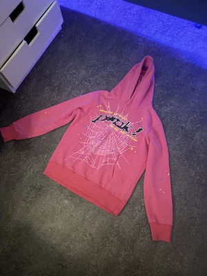 Pink spider hoodie - Brand: Sp5der (Spider) Type: Hoodie Color: Pink  Description: Pink Sp5der hoodie in good condition. Soft and comfortable with a hood and ribbed cuffs. Small logo on the front and a large spider web graphic with “Sp5der” text and colorful star details on the back.  Condition: No holes or major stains. Only normal wear.  Style: Perfect for streetwear / everyday use.