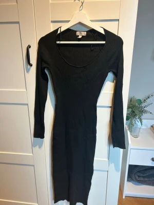Svart ribbad stickad långklänning - Säljer en svart långklänning med ribbad struktur och lång ärm. Klänningen har en rundad urringning och sitter tight mot kroppen. Det är även en slit längst ut på armarna som en snygg detalj. Materialet är stickat och stretchigt, vilket gör den både bekväm och snygg. Se tredje bilden för längdreferens, jag är 161. Klänningen är använd två gånger.