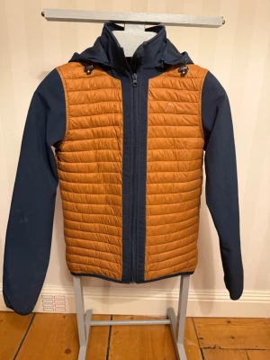 Orange och marinblå pufferjacka Equipage - Säljer en orange och marinblå pufferjacka från Equipage. Jackan har quiltad kropp, släta ärmar och huva. Stängs med dragkedja framtill och har en sportig look. Perfekt för dig som vill ha en lätt och snygg jacka till vardags.