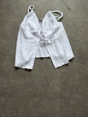 Vit omlottopp från Amisu XS - Säljer en vit omlottopp från Amisu i storlek XS. Toppen har tunna axelband, v-ringning och knyt framtill. Tröjan är helt öppen framtill. Materialet är lätt och har en krinklad struktur. Perfekt till sommaren och enkel att styla med jeans eller kjol. Tröjan har aldrig använts.