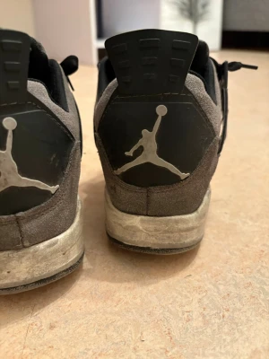 Svarta Nike Air Jordan 4 sneakers - Säljer ett par svarta Nike Air Jordan 4 sneakers i mocka med klassisk Jumpman-logga på häl och plös. Skorna har snörning, meshdetaljer på sidorna och en robust sula. Perfekta för dig som gillar streetwear och vill ha en ikonisk sneaker i garderoben.