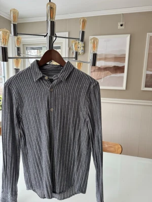 Randig skjorta Zara - Säljer en långärmad skjorta från Zara i grått med tunna vita ränder. Skjortan har klassisk krage, knäppning framtill och är tillverkad i mjuk bomull. Storlek S, skriv för frågor och funderingar!