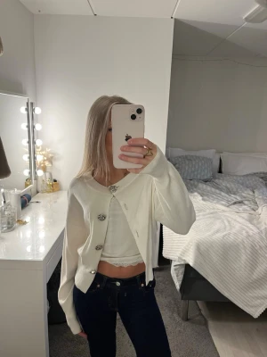 Vit kofta med dekorativa knappar - Säljer en söt vit kofta med stora dekorativa knappar. Koftan är stickad och har en lite loose passform med långa ärmar. Perfekt att slänga över ett linne eller topp för en chill look.