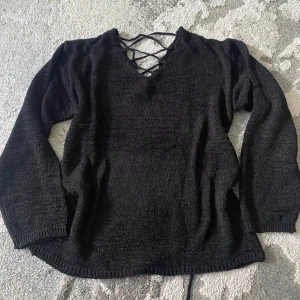 Lewkin drop shoulder svart stickad tröja med snörning på baksidan - Svart stickad tröja med snygg snörningsdetalj både bak på ryggen som kan tas ut och ha en liten öppen rygg. Tröjan har v-ringning och långa ärmar, och kan bäras offshoulder för en avslappnad vibe. Ny och aldrig använd och har originals paketet fortfarande
