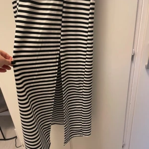 Randig långklänning från Sinsay - Svartvit långklänning från Sinsay med horisontella ränder, v-ringad omlott-topp och resår i midjan. Klänningen har korta ärmar och är tillverkad i mjuk bomull, perfekt för en chill och stilren look.