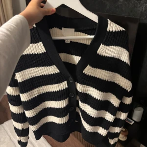 Randig svartvit kofta från H&M - Säljer en ribbstickad kofta från H&M med breda svarta och vita ränder. Koftan har v-ringning, knappar framtill och långa ärmar. Endast testat den.