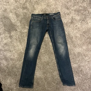 Replay Dave Comfort Fit jeans blå - Snygga Replay Dave Comfort Fit jeans i mörkblå tvätt med lätt slitna detaljer. Klassisk femficksmodell, raka ben och normal passform. Mjukt och flexibelt jeanstyg som sitter skönt hela dagen. Perfekt för dig som gillar stilrena och bekväma jeans.
