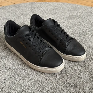 Svarta sneakers med vit sula - Svarta sneakers med stilren design och vit sula. Skorna har snörning, rund tå och är tillverkade i skinn. Diskret guldtext på sidan och logga bak på hälen. Perfekta för dig som gillar minimalistisk och clean stil.