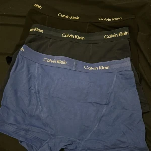 Calvin Klein boxershorts 3-pack - Säljer ett 3-pack klassiska boxershorts från Calvin Klein i svart och blått. De har en elastisk midja med logotyp, tight passform och är tillverkade i mjuk bomull för maximal komfort. Perfekta för dig som gillar stilrena och bekväma underkläder. De är oanvända 