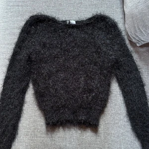 Svart fluffig stickad tröja Divided - Mysig svart stickad tröja från Divided i storlek 38. Tröjan har en fluffig och lite lurvig textur som ger en cool look. Långärmad och perfekt för kyligare dagar. Passar dig som gillar en trendig och bekväm stil.