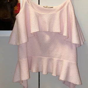 Ljusrosa volangtop från Nelly XS - Supersöt ljusrosa topp från Nelly i storlek XS. Toppen har breda volanger både upptill och nedtill, vilket ger en flowy och feminin look. Materialet är strukturerat och känns mjukt mot huden. Perfekt för dig som gillar romantiska vibes och vill sticka ut.