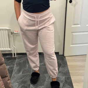 Ljusrosa mjukisbyxor med snörning - Säljer ett par ljusrosa mjukisbyxor med elastisk midja och snörning framtill. Byxorna har ribbade muddar vid bensluten och en loose passform som är riktigt chill. Perfekta för att hänga hemma eller dra till gymmet. Supermjukt material i bomull.