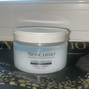 NeoLumo Ocean Body Scrub 300ml - Fräsch body scrub från NeoLumo med havsinspirerad doft, berikad med vitamin C och E. Kommer i en rund plastburk med vitt lock och ljusblått innehåll. Perfekt för att exfoliera huden och ge en mjuk känsla. Volymen är 300 ml.