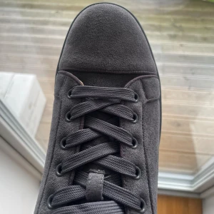 Christian Louboutin  - Säljer ett par gråa sneakers från Christian Louboutin i mjuk mocka med klassisk röd sula. Skorna har rund tå, platt sula och snörning framtill. Snygg och stilren design som sticker ut med den ikoniska röda undersidan. Skickas med original box och allting i.