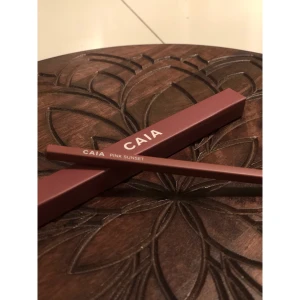 CAIA Pink Sunset läppenna - Snygg läppenna från CAIA i färgen Pink Sunset. Pennan har en mjuk, rosabrun ton som passar perfekt för att definiera läpparna. Kommer i en stilren, vinröd förpackning med vit logga. Träpennan är lätt att vässa och har en klassisk spetsig form.