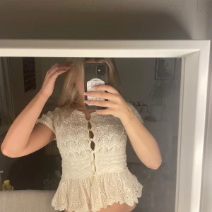 Vit spetsblus med volang och knappar - Superfin vit blus med korta ärmar, spetsdetaljer och volang nedtill. Blusen har dekorativa knappar framtill och ett broderat mönster.  klippte tyvärr bort kappen innan jag provade den så den är enbart provad