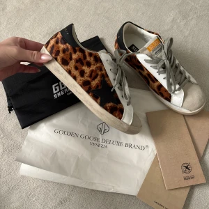 Golden Goose sneakers leopardmönster - Golden Goose sneakers med leopardmönstrade sidor, svarta detaljer och vit skinnpanel. Grå snörning, beige mockatå och svart häl med guldfärgad logga. Snygg platt sula och ikonisk stjärndetalj på sidan. Perfekta för dig som vill sticka ut. Aldrig använda då jag fick dem i present och de var i fel stl