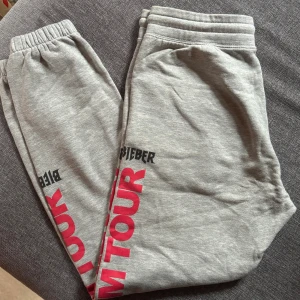 Grå Team Bieber mjukisbyxor S - Grå mjukisbyxor från Team Bieber med tryck i rött och svart längs benet. Byxorna har resår i midjan och är gjorda i mjuk bomullsmix, perfekta för en avslappnad stil. Snygg detalj med 'Purpose Tour' tryck på benet.