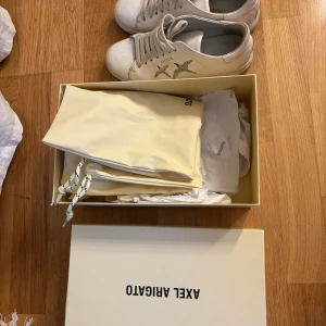 Vita sneakers med fåglar från Axel Arigato - Snygga vita sneakers från Axel Arigato med broderade fåglar på sidan. Skorna har snörning, rund tå och platt sula. Tillverkade i skinn och levereras med originalkartong och dustbags. Perfekta för en stilren och modern look. Jag hittar även inte dessa skor längre så antar att de inte säljs längre. 