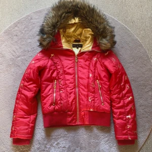 Äkta vintage 2000s y2k BabyPhat pufferjacka - Säljer en äkta vintage pufferjacka från märket Baby Phat! Snygg röd jacka med guldiga detaljer och mönster. Jackan har en stor huva med fuskpäls, dragkedja framtill, ribbade muddar och två fickor med guldfärgade dragkedjor! Insidan är guldfärgad satin och jackan har coola spänndetaljer på huvan baktill 😻 Har även en innerficka, där något skärt tyget så en liten defekt där (men fixas med nål & tråd)!! Pälsen är avtagbar 🙌🏼 Använd någon gång. Storlek M, men passar XS-S också 💕 Pris kan diskuteras!❤️