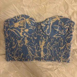Blå och vit bandeau tubtopp från Zara - Supersnygg bandeau tubtopp från Zara i blått och vit med abstrakt mönster. Toppen är smockad och har kupor för extra stöd. Perfekt att styla med höga jeans eller kjol för en trendig look.