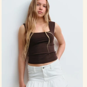 Brun croppad linnetopp - Snygg brun croppad linnetopp med breda axelband och fyrkantig halsringning. Toppen är ärmlös och har en tight passform som framhäver siluetten. Perfekt för dig som gillar minimalistisk stil och vill ha en enkel men trendig topp. Topp i storlek 170, passar mig som är xs och s. Helt ny utan prislapp 