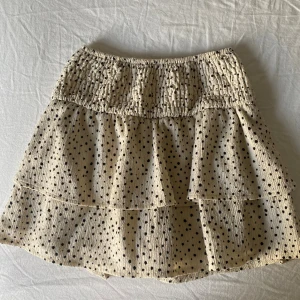 Prickig volangkjol från Zara -  Storlek 152cm men passar XS och har shorts under. Supersöt kort volangkjol från Zara i beige med svarta prickar. Kjolen har smock i midjan och två lager volanger som ger en luftig och lekfull känsla. Perfekt för dig som gillar en trendig och avslappnad stil.