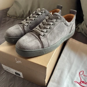 Louboutins - Snygga grå sneakers från Christian Louboutin i mjuk mocka med matchande grå snörning och platt sula. Skorna har en stilren design med rund tå och diskreta detaljer, perfekt för dig som gillar exklusiva och minimalistiska sneakers.