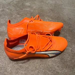 Puma Ultra orange fotbollsskor 40.5 - Säljer ett par grymt snygga Puma Ultra fotbollsskor i en riktigt skrikig orange färg. Skorna har snörning, metall-dobbar och en aerodynamisk form med Pumas logga på sidan. Ovandelen är i lätt syntetmaterial för maxad fart på planen.