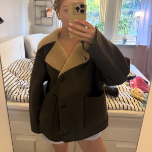 Brun teddyjacka med stora fickor - Mysig brun teddyjacka från Zara med stora fickor och bred krage i beige fuskpäls. Jackan har knäppning med svarta knappar och en oversized passform. Perfekt för kalla dagar när du vill vara både varm och snygg. En av knapparna har blivit lite lösa men det finns en extra knapp man kan sätta på ifall något skulle hända/knappen skullle lossna (se 2 sista bilderna). Storlek XS men sitter som en S/M Jag köpte den för 1200kr 🥰