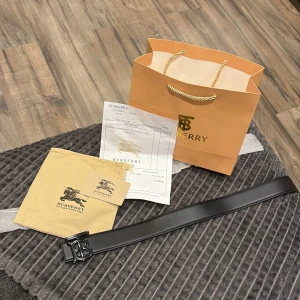 Svart Burberry skärp i skinn - Snyggt svart Burberry bälte i skinn med stilren TB-logga i metall som spänne. Bältet har en klassisk, rak form och kommer med originalpåse och Burberry shoppingbag. Perfekt för att lyfta din outfit med en lyxig touch.