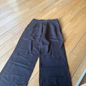 Svarta wide chinos med fickor - Snygga svarta chinos med breda ben och klassisk passform. Byxorna har framfickor och två bakfickor med knappstängning. Perfekta för dig som gillar en avslappnad och stilren look. Materialet känns mjukt och lätt, och midjan har hällor för bälte.