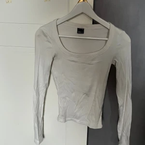 Vit ribbad långärmad topp Gina Tricot - En basic vit långärmad topp från Gina Tricot med ribbad struktur och rundad urringning. Sitter tight och är perfekt att styla med jeans eller kjol. Enkel och stilren design som funkar till många olika looks.
