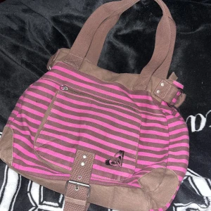 Y2K axelväska - Snygg väska från Roxy i brunt och rosa. Har en ficka fram, bak och en extra ficka inuti. Mycket bra skick!