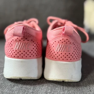 Nike rosa sneakers med vit sula - Säljer ett par snygga rosa Nike sneakers i storlek 38. Skorna har vit sula med synlig luftbubbla, perforerade detaljer bak och klassisk snörning. Ovandelen är i syntetmaterial och mesh för extra komfort. Perfekta för dig som vill sticka ut med färg på fötterna.