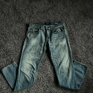 Replay blå jeans straight fit - Säljer ett par klassiska blå jeans från Replay med straight fit och normal passform. Jeansen har slitna detaljer framtill, fem fickor och läderpatch bak. Materialet är robust denim i bomull och färgen är ljusblå med tvättad look.